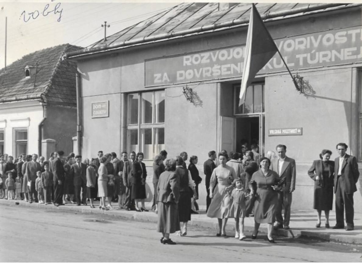 So zaujímavou fotografiou sa podelil pán Vladimír Sušanin. Fotograf zachytil zástup ľudí čakajúcich na možnosť hodiť hlasovací lístok vo voľbách do Národného zhromaždenia Č-SSR, SNR a do Národných výborov 12. júna 1960. Budova bola vtedy známa ako Dom osvety, no napr. v roku 1938 tu bolo Púchovčanom oznámené, že v Žiline bola 6. októbra vyhlásená autonómia Slovenskej krajiny. Pred 80 rokmi sa budova na rohu dnešného Námestia slobody a Mozesovej (pešej) ulice pod vežou kostola volala Katolícky kultúrny dom.